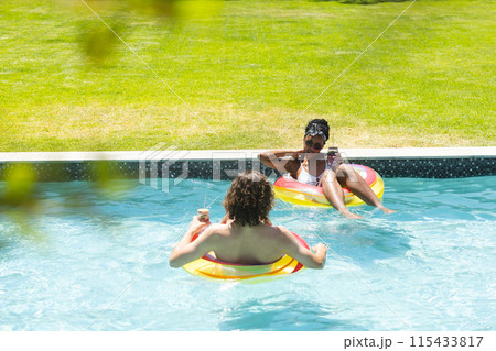 Diverse couple young African American woman and Caucasian man relax on floaties in a pool Diverse couple young African American woman and Caucasian man relax on floaties in a pool 115433817