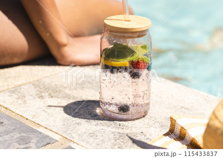 A clear water bottle with lemon and berries sits by a poolside A clear water bottle with lemon and berries sits by a poolside 115433837
