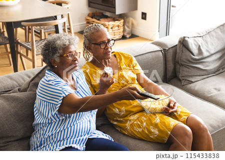 Senior African American woman and senior biracial woman enjoy a movie together, sharing popcorn Senior African American woman and senior biracial woman enjoy a movie together, sharing popcorn 115433838