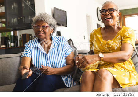Senior African American woman and senior biracial woman sit together on a couch at home 115433855