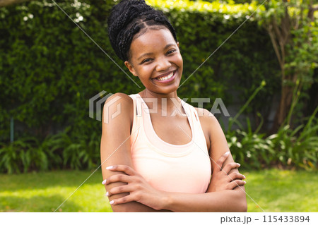 Young African American woman smiles brightly, arms crossed in a casual peach top 115433894
