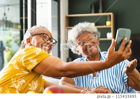 Senior African American woman and senior biracial woman are smiling while taking a selfie at home Senior African American woman and senior biracial woman are smiling while taking a selfie at home 115433895