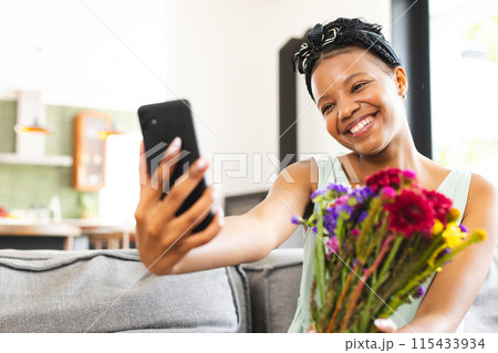 Young African American woman takes a selfie with a bouquet of colorful flowers with copy space 115433934