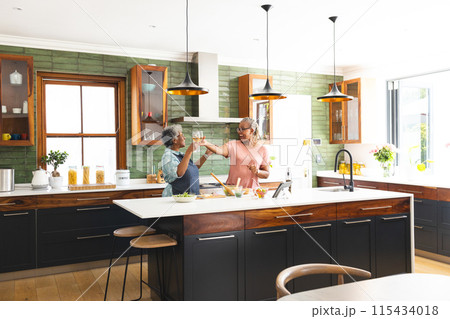 Senior African American woman and senior biracial woman toast in a bright kitchen Senior African American woman and senior biracial woman toast in a bright kitchen 115434018