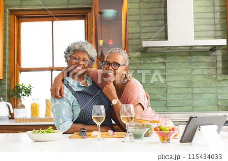 Senior African American woman and senior biracial woman share a warm embrace in a kitchen Senior African American woman and senior biracial woman share a warm embrace in a kitchen 115434033