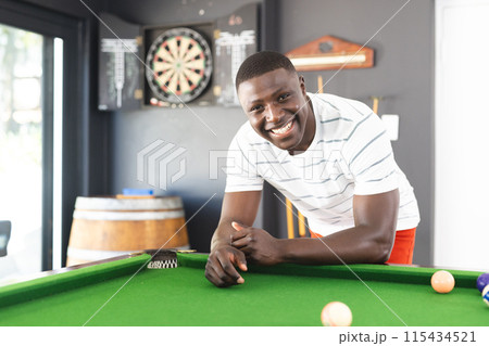 Young African American man smiles while leaning on a pool table 115434521