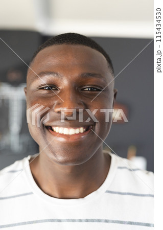 A young African American man smiles brightly, wearing a white striped shirt 115434530