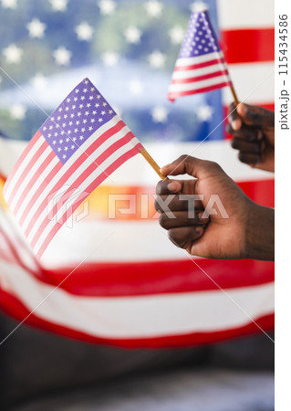 Two hands wave small American flags against a blurred background Two hands wave small American flags against a blurred background 115434586
