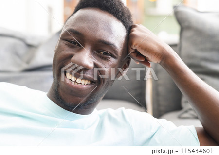 Young African American man smiles broadly, showcasing a casual style in a light blue shirt 115434601