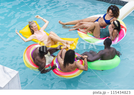 Diverse group of friends enjoys a pool day, floating on colorful rings Diverse group of friends enjoys a pool day, floating on colorful rings 115434823
