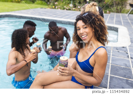 Biracial woman in blue swimwear enjoys a drink by the pool with diverse friends Biracial woman in blue swimwear enjoys a drink by the pool with diverse friends 115434892