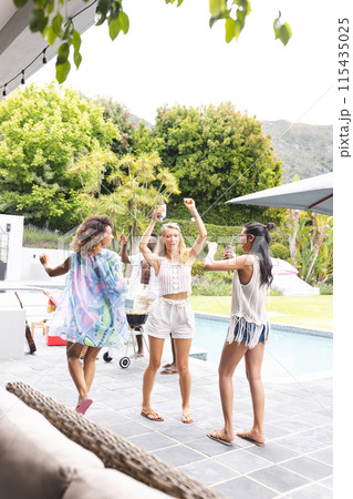 Three women dance joyfully outdoors near a pool, raising their glasses in celebration Three women dance joyfully outdoors near a pool, raising their glasses in celebration 115435025