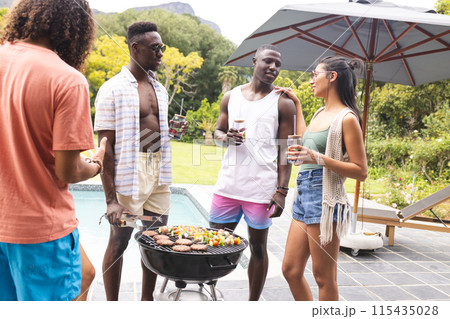 Diverse friends enjoy a barbecue outdoors, with a young African American man at the grill 115435028