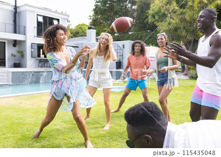 Diverse group of friends enjoy a game of football in a sunny backyard 115435048
