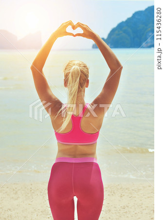 Fitness, yoga and heart hands with woman on beach for wellness, mental health or exercise in nature. Environment, spiritual peace and athlete back doing warm up, zen wellbeing and ocean workout 115436280