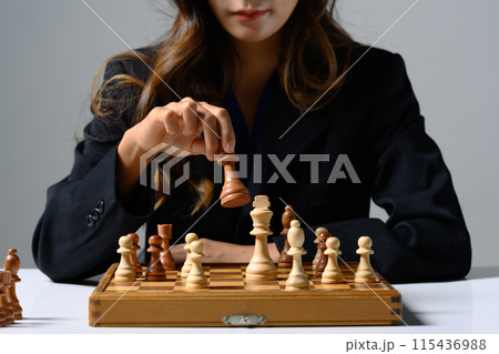 Businesswoman moving a chess piece on a chess board. Business competition strategy and management concept Businesswoman moving a chess piece on a chess board. Business competition strategy and management concept 115436988