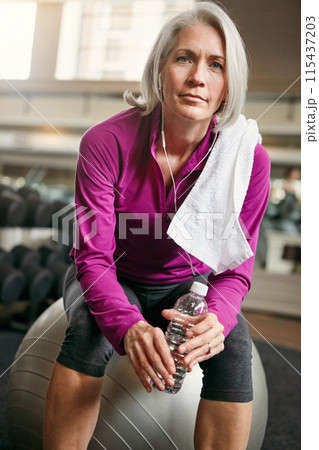 Relax, portrait of mature woman with workout, fitness and pride with water bottle on gym ball. Exercise, training and confident female athlete on break with earphones, health and wellness in club. 115437203