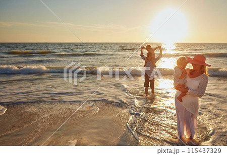 Family, parents and beach with children in sunset for bonding, outdoor holiday or weekend in nature. Mom, father or kids playing together for embrace, love or care in sunshine by ocean coast or sea 115437329