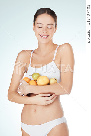 Happy woman, fruit and underwear in studio for health, diet and nutrition on white background. Female nutritionist, food and hands with smile for wellness, self care and vitamins for wellbeing 115437483