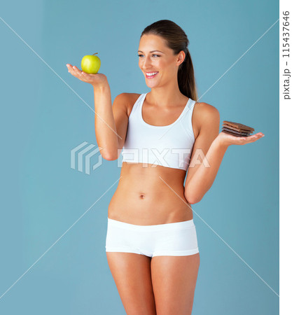 Smile, woman and chocolate with apple food choice isolated on studio, sugar and diet in blue background. Dessert, young vegetarian person for detox and green fruit, lose weight decision or vegan 115437646
