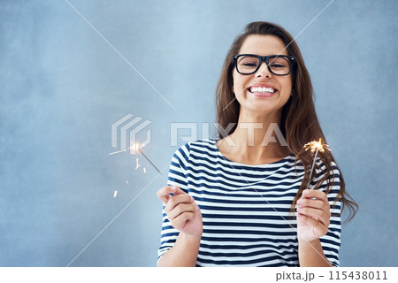 Portrait, happiness and woman in studio with sparklers isolated on blue background for celebration. Glasses, light and fun birthday event or new year with glow, vision and fireworks with confidence. 115438011