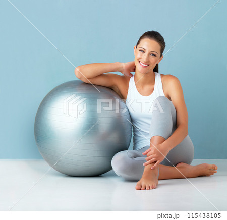 Fitness, happy woman and exercise ball in portrait on floor for core workout, balance and rest in studio. Smile and female person with training equipment for health, weight loss and blue background Fitness, happy woman and exercise ball in portrait on floor for core workout, balance and rest in studio. Smile and female person with training equipment for health, weight loss and blue background 115438105