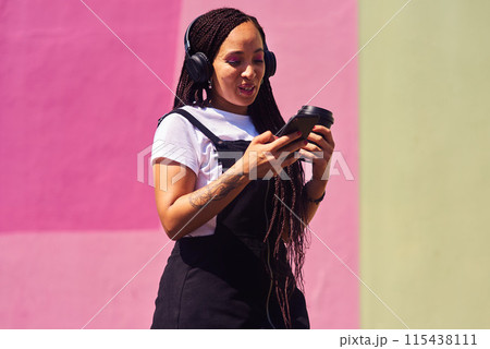Woman, phone and outdoor for podcast and coffee, streaming music and subscription by wall background. Female person, latte and listening to podcast or online for social media, song and travel in city 115438111
