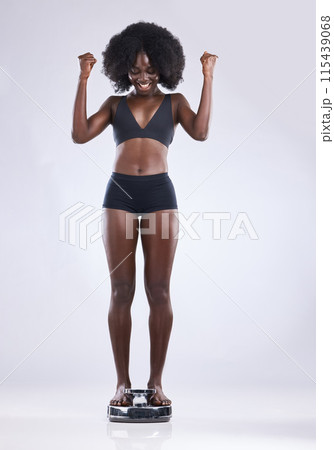 Fitness, scale and black woman with winner fist in studio celebration for weight loss, progress or calorie goals on white background. Wow, body or African model excited for bmi, target or success 115439068
