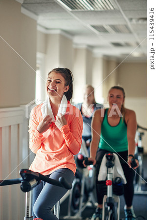 Happy woman, cycling and towel with spin class for fitness, training or workout exercise at indoor gym. Active female person or group of cyclists with smile on equipment or bicycle at health club Happy woman, cycling and towel with spin class for fitness, training or workout exercise at indoor gym. Active female person or group of cyclists with smile on equipment or bicycle at health club 115439416