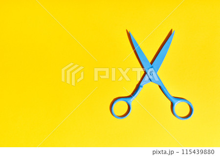Bright blue scissors over yellow background with copy space 115439880