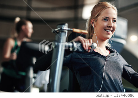 Gym, woman and happy on chest press machine for workout to exercise for health, fitness and muscles. Female person, smile and earphones with training for wellbeing, wellness and self care in routine 115440086