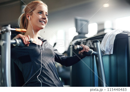 Gym, woman and happy on chest press machine for workout to exercise for health, fitness and muscles. Female person, smile and earphones with training for wellbeing, wellness and self care in routine 115440483
