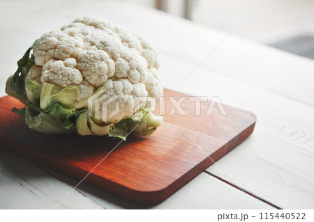 Cauliflower, wood board and cooking in kitchen for health, lunch and choice for nutrition with wellness. Organic vegetable, cooking and chopping block on table, leaves and meal prep for vegan diet 115440522
