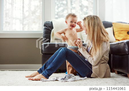 Home, portrait and dressing of baby by mom, living room and playful with son, love and care in apartment. House, mother and toddler in lounge, clothes and fun together, happiness and wellness for boy Home, portrait and dressing of baby by mom, living room and playful with son, love and care in apartment. House, mother and toddler in lounge, clothes and fun together, happiness and wellness for boy 115441061