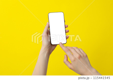 Female hand holding a smartphone on a yellow background Female hand holding a smartphone on a yellow background 115441545