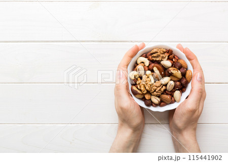 Woman hands holding a wooden bowl with mixed nuts Walnut, pistachios, almonds, hazelnuts and cashews. Healthy food and snack. Vegetarian snacks of different nuts Woman hands holding a wooden bowl with mixed nuts Walnut, pistachios, almonds, hazelnuts and cashews. Healthy food and snack. Vegetarian snacks of different nuts 115441902