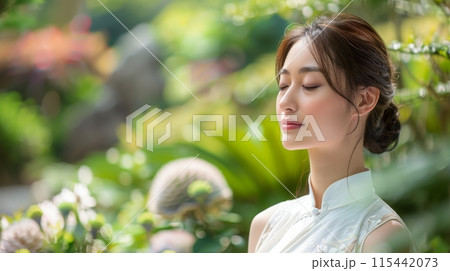 A woman wearing a traditional white dress with hair tied up practicing mindfulness against a blurred natural background 115442073