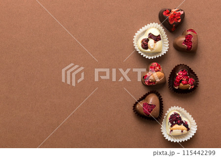 chocolate sweets in the form of a heart with fruits and nuts on a colored background. top view with space for text, holiday concept chocolate sweets in the form of a heart with fruits and nuts on a colored background. top view with space for text, holiday concept 115442299