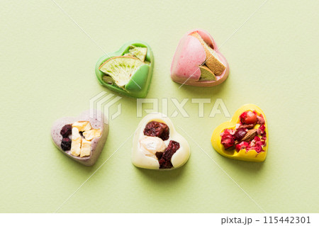 chocolate sweets in the form of a heart with fruits and nuts on a colored background. top view with space for text, holiday concept chocolate sweets in the form of a heart with fruits and nuts on a colored background. top view with space for text, holiday concept 115442301