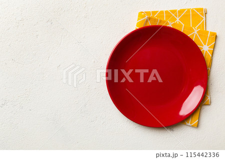 Top view on colored background empty round red plate on tablecloth for food. Empty dish on napkin with space for your design 115442336