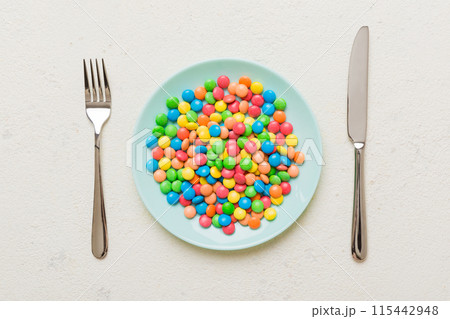 cutlery on table and sweet plate of candy. Health and obesity concept, top view on colored background 115442948
