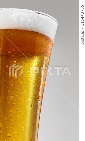 Close-up of pint glass filled with golden, craft beer topped with frothy foam against grey studio background. Close-up of pint glass filled with golden, craft beer topped with frothy foam against grey studio background. 115443735