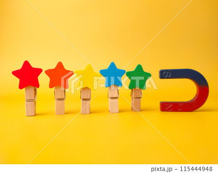 Colored wooden star attract by magnet on a yellow background. 115444948