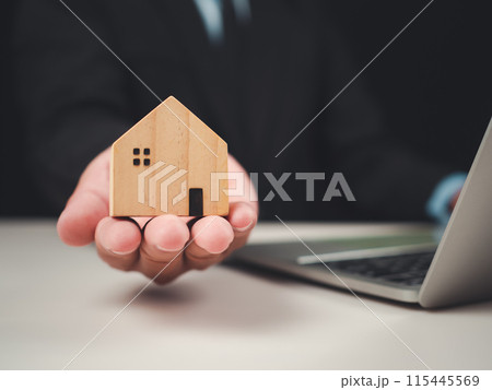 Businessman shows off a model wooden house It represents a real estate agent offering a house, Offers information about homes and purchases Real estate trading concepts, Real estate business. 115445569