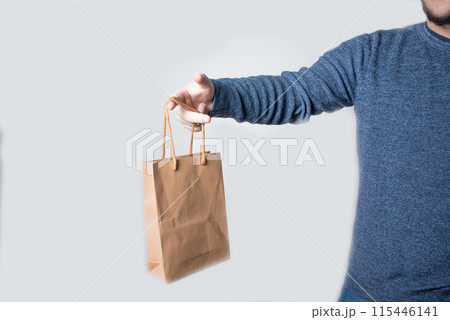 Young anonymous adult dressed with jeans and pullover delivering a brown paper bag 115446141