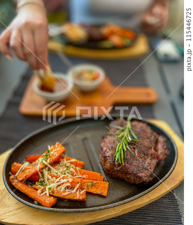 Grilled Steaks with spices rosemary and pepper on wooden board on black background. 115446725