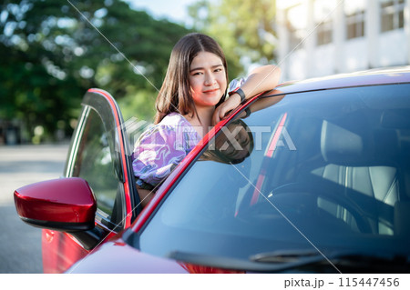 Portrait asian woman Wear purple dress wearing smartwatch in the car door modern red car at the city park outdoors. Portrait asian woman Wear purple dress wearing smartwatch in the car door modern red car at the city park outdoors. 115447456