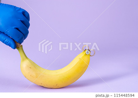 Intimate piercing. Minimal piercing concept. Banana with piercing on purple background Intimate piercing. Minimal piercing concept. Banana with piercing on purple background 115448594