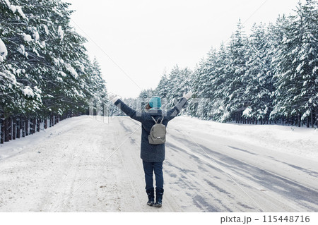a girl in a gray coat with a gray backpack on her back, walks along the side of a winter road, 115448716