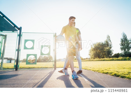 Two Young Caucasian Men Playing Basketball at the Park outdoor playground in sunset light. Teenagers' hobby, offline activity. Concept of sports, hobbies and healthy lifestyle. Selective focus. Two Young Caucasian Men Playing Basketball at the Park outdoor playground in sunset light. Teenagers' hobby, offline activity. Concept of sports, hobbies and healthy lifestyle. Selective focus. 115448981